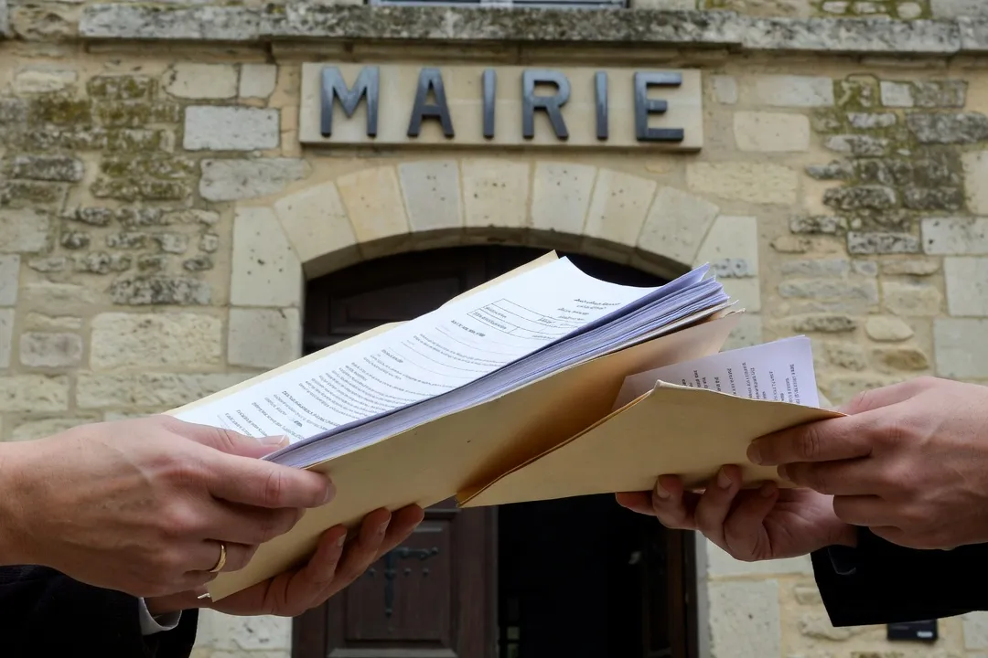 Couple’s hands holding a folder of legal documents near a French mairie building
